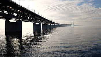 A stunning view of a large steel bridge reflecting on the tranquil water under a cloudy sky. HD wallpaper