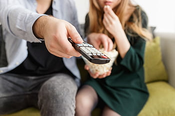 A couple enjoying a relaxing movie night, sitting on a sofa with popcorn and a TV remote. HD wallpaper