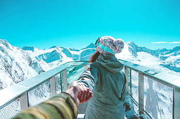 A woman in winter clothing holds a hand and walks on a scenic snow-covered mountain deck in Zell am See. HD wallpaper