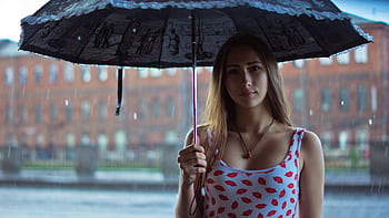 A young woman stands outdoors holding an umbrella in the rain, creating a moody portrait. HD wallpaper