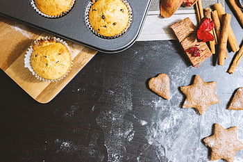 A delicious arrangement of muffins and cookies with cinnamon and flour on a black countertop. HD wallpaper