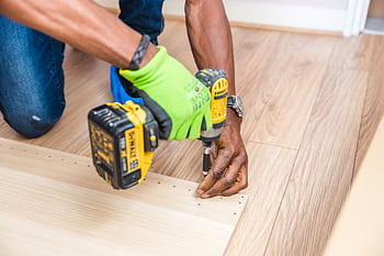 Close-up of handyman drilling wood indoors with green gloves and cordless drill. HD wallpaper