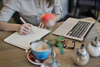 Woman writing in a notebook with a laptop and coffee cup on a desk. Ideal for workspace inspiration. HD wallpaper