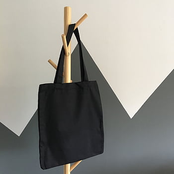 Simple and elegant black canvas tote bag hanging on a wooden rack, perfect for eco-friendly shopping. HD phone wallpaper