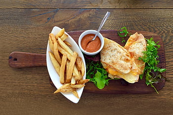 Delicious grilled cheese sandwich with crispy fries and a side of dipping sauce on a wooden table. HD wallpaper