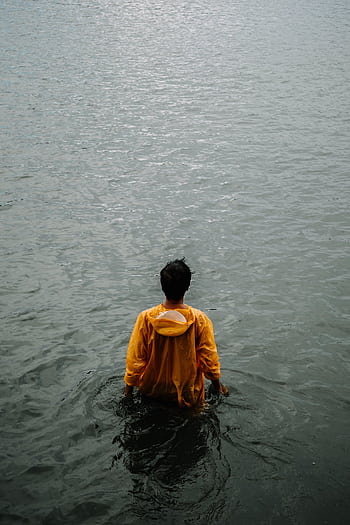 An individual in a yellow jacket stands alone in water, conveying solitude. HD phone wallpaper