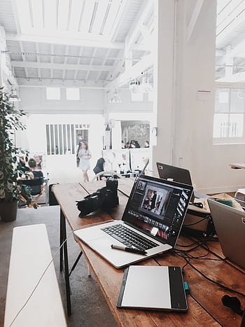 A bright, modern workspace featuring laptops, a camera, and a drawing tablet in an indoor office. HD phone wallpaper