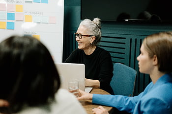 Smiling senior businesswoman leading a diverse team meeting in an office. HD wallpaper