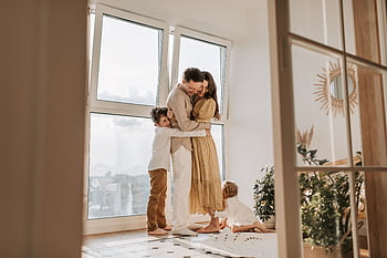 A happy family embracing near a large window in a bright, cozy room filled with natural light. HD wallpaper