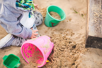 A child enjoys playing in a sandbox using vibrant colored buckets during a sunny day. HD wallpaper