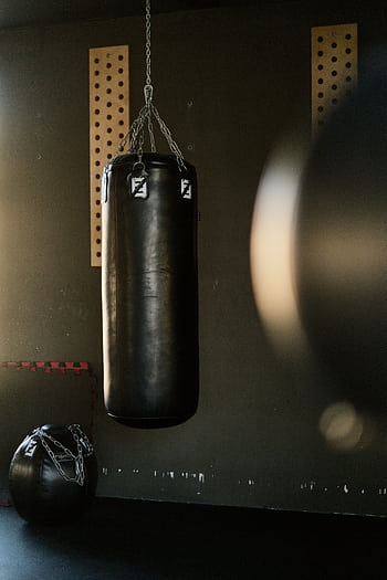 Black punching bag hangs in a gym, bathed in sunlight, creating a moody and focused atmosphere. HD phone wallpaper