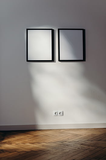 Two black frames casting shadows on a white wall in a sunlit room with wooden flooring. HD phone wallpaper