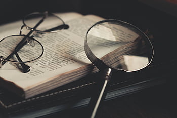 Detailed close-up of an open book with a magnifying glass and eyeglasses, emphasizing discovery and exploration. HD wallpaper