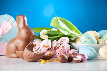 A vibrant Easter display featuring a chocolate bunny, pastel eggs, and tulips. HD wallpaper
