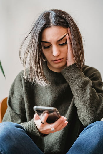 Young woman inside looking concerned while reading her smart. HD phone wallpaper
