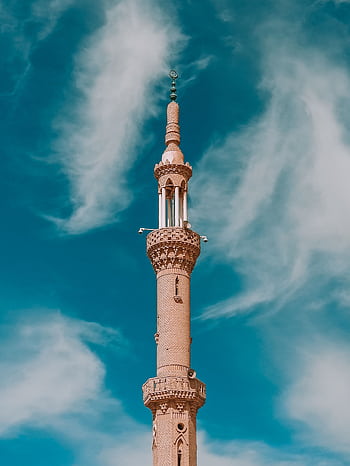 A tall, intricately designed Islamic minaret set against a vibrant blue sky with clouds, showcasing architectural beauty. HD phone wallpaper