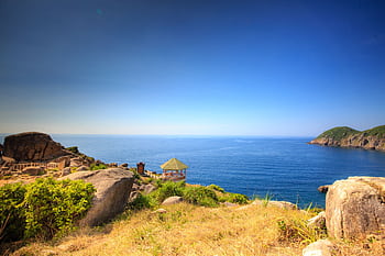Peaceful seaside view with rocks, green hills, and blue sky. Perfect for nature lovers. HD wallpaper
