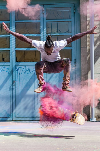 Skateboarder jumps in vibrant pink powder cloud capturing urban street art vibe. HD phone wallpaper