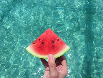 Hand holding a ripe watermelon slice with a turquoise pool background, perfect summer vibes. HD wallpaper
