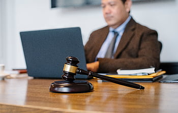 A professional lawyer in a formal setting working on a laptop with a gavel in focus on the desk. HD wallpaper