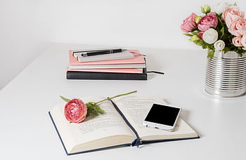 A stylish home office setup with open book, smart, and flowers on a white desk. HD wallpaper