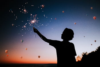 Silhouette of a person holding sparklers against a colorful twilight sky. HD wallpaper