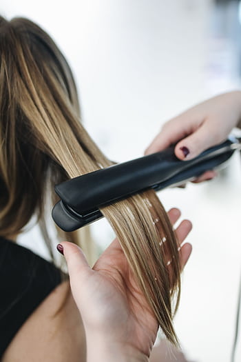 Close-up of a hairstylist using a flat iron on blonde hair in a salon setting. HD phone wallpaper