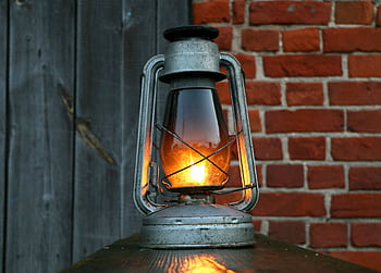 Close-up of an antique oil lantern casting a warm glow against a rustic red brick wall. HD wallpaper