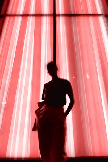 Artistic silhouette of a person standing against a blurred neon pink light display. HD phone wallpaper