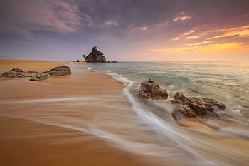Tranquil beach scene at sunrise with soft waves and rock formations. HD wallpaper
