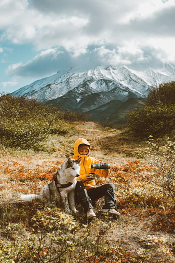 Person enjoying a break with a Siberian Husky in a stunning mountain landscape. HD phone wallpaper