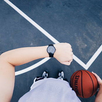 A basketball player checks their wristwatch while holding a ball on an outdoor court. HD phone wallpaper