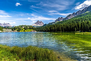 Scenic view of a tranquil alpine lake with towering mountain peaks and lush forests in the Dolomites. HD wallpaper