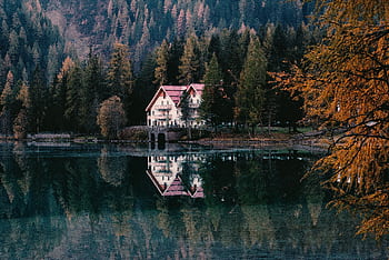 Tranquil lakeside house surrounded by vibrant autumn forest reflections. HD wallpaper