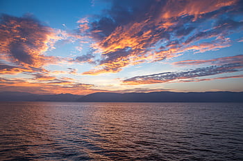 A vibrant sunset with dramatic clouds reflects over the calm ocean, capturing nature's beauty. HD wallpaper