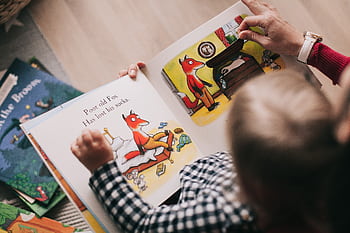 A child and adult reading an illustrated storybook together in a cozy setting. HD wallpaper