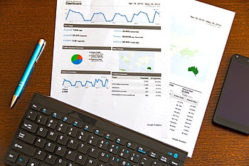 Flatlay of a business analytics report, keyboard, pen, and smart on a wooden desk. HD wallpaper