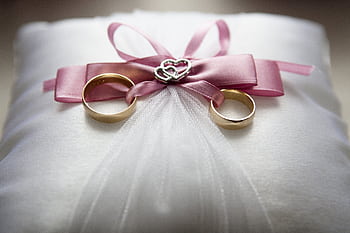 Close-up of elegant wedding rings on a silk pillow with a pink ribbon and a heart decoration, symbolizing love. HD wallpaper