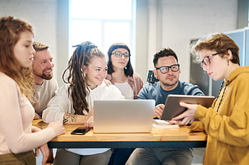 A diverse group of professionals engaged in a brainstorming session around a wooden table with technology present. HD wallpaper