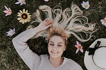 A smiling woman with closed eyes lies on grass, surrounded by flowers, capturing a moment of pure relaxation. HD wallpaper