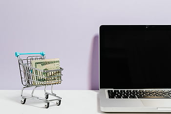 Shopping cart with money next to a laptop symbolizing online shopping and e-commerce. HD wallpaper